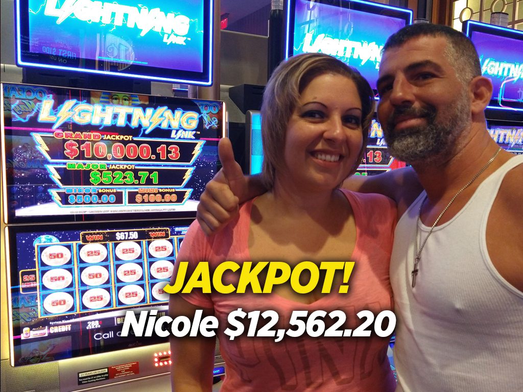 A woman and man posing for the camera in front of a slot machine.
