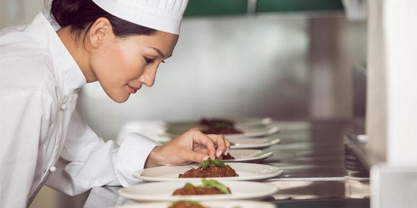 A woman in chef 's hat preparing food on plates.