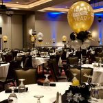 A banquet hall with tables and chairs, white table cloths, black tablecloth, and balloons.