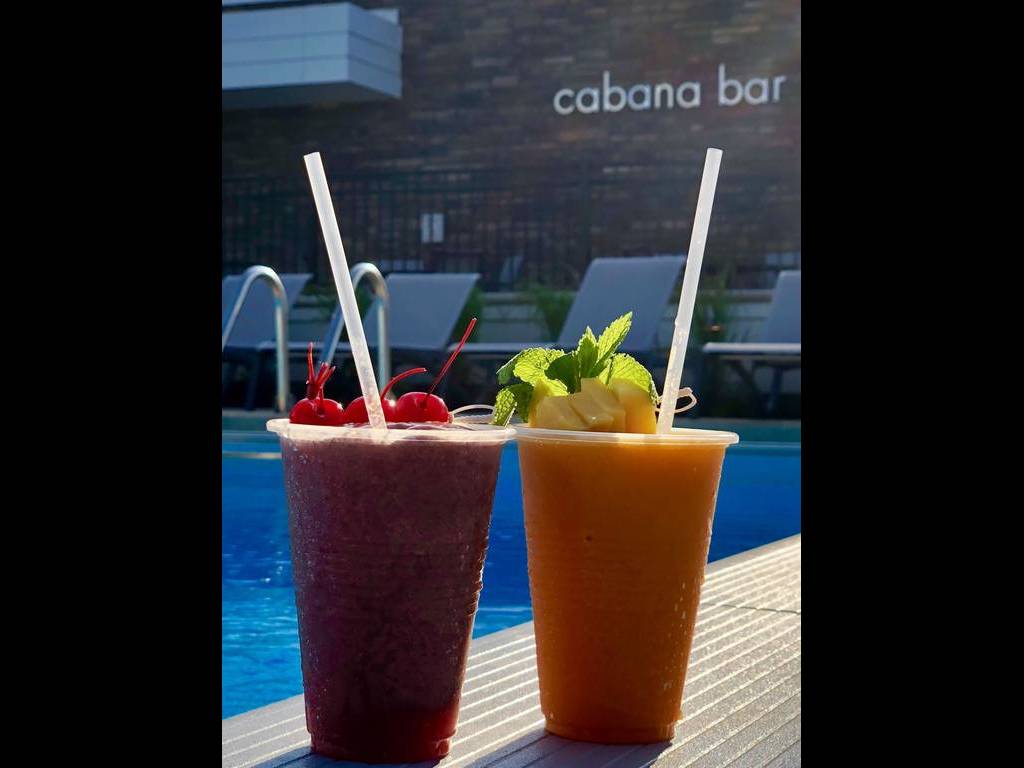 Two drinks are sitting on the edge of a pool.