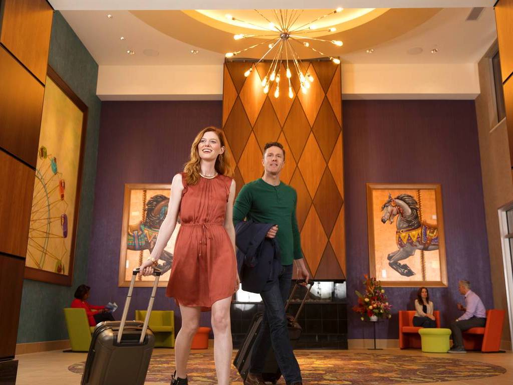Two people walking in a lobby with luggage.