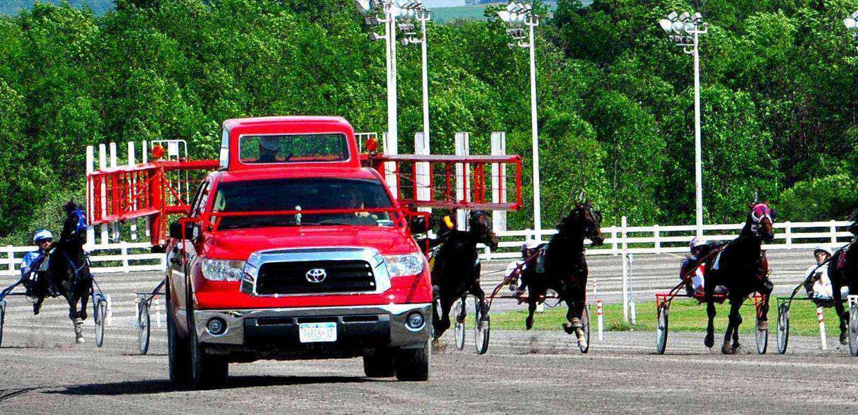 A red truck pulling two horses in front of a fence.