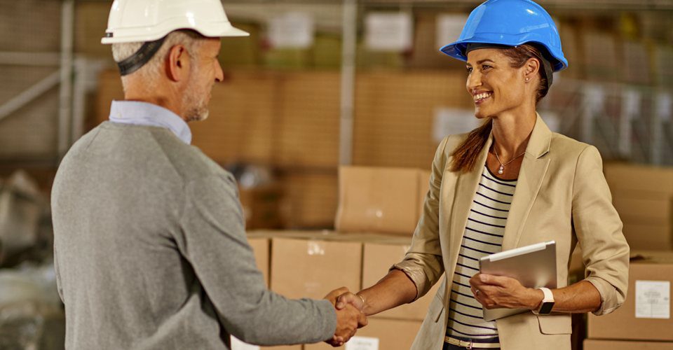 A man and woman shaking hands in front of boxes.