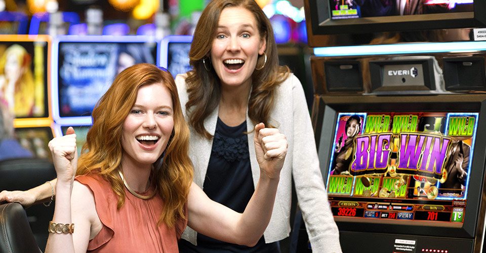 Two women are posing for a picture in front of some slot machines.