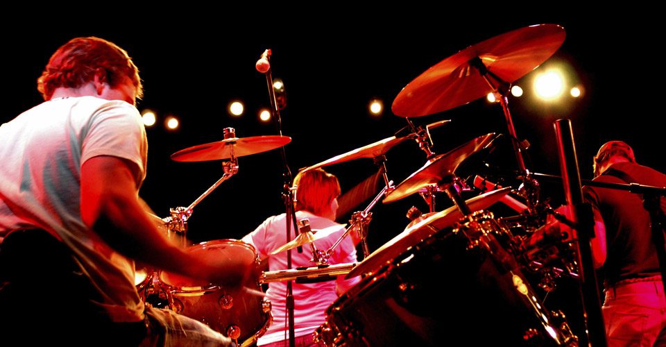 A man playing drums on stage with other musicians.